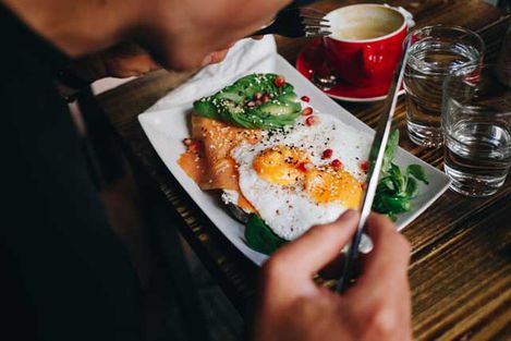 Behind the shoulder shot of man enjoying healthy and delicious tasty breakfast or weekend brunch at trendy popular cafe. Sunny side up eggs with salmon and avocado. Food blogger inspiration