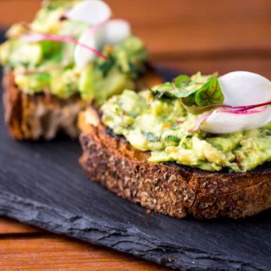 Avocado Toast. Classic American Diner Breakfast or Brunch Restaurant menu item: avocado toast. Made w/ fresh avocados smashed into guacamole and chopped tomatoes with salt and pepper served on toast.